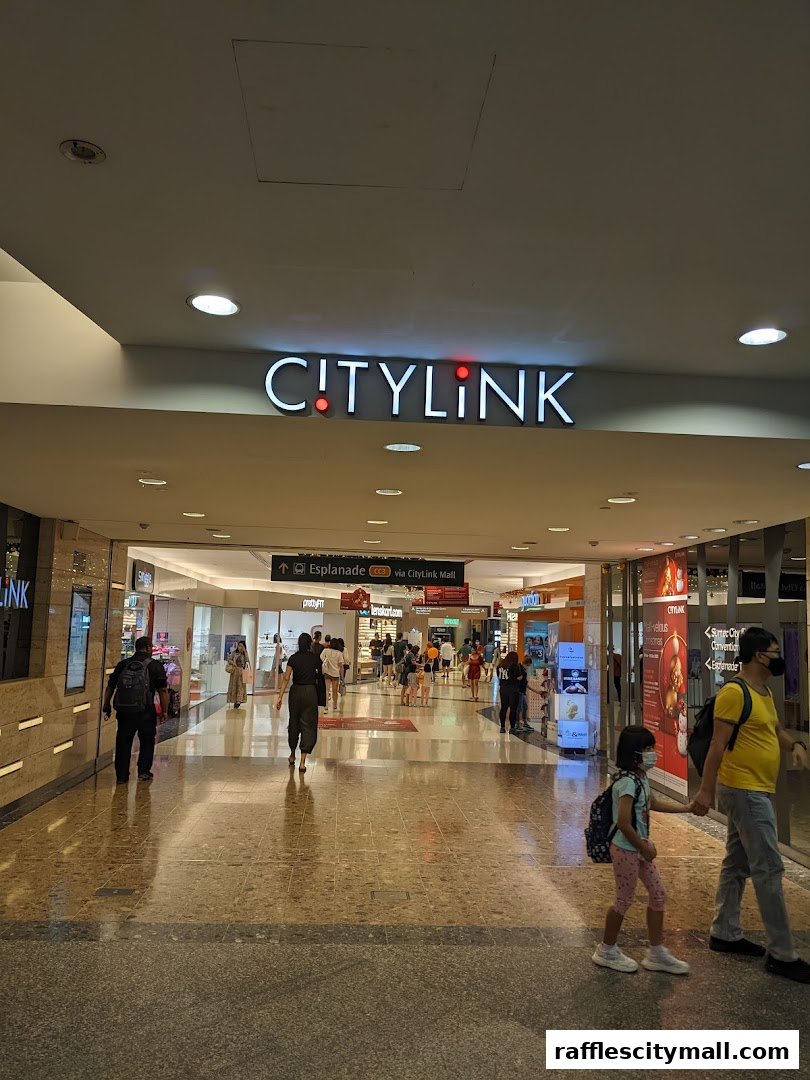 People walking through a brightly lit shopping mall corridor with various shops visible.