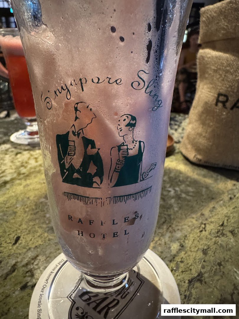 A close-up of a Singapore Sling cocktail in a glass with the Raffles Hotel logo.