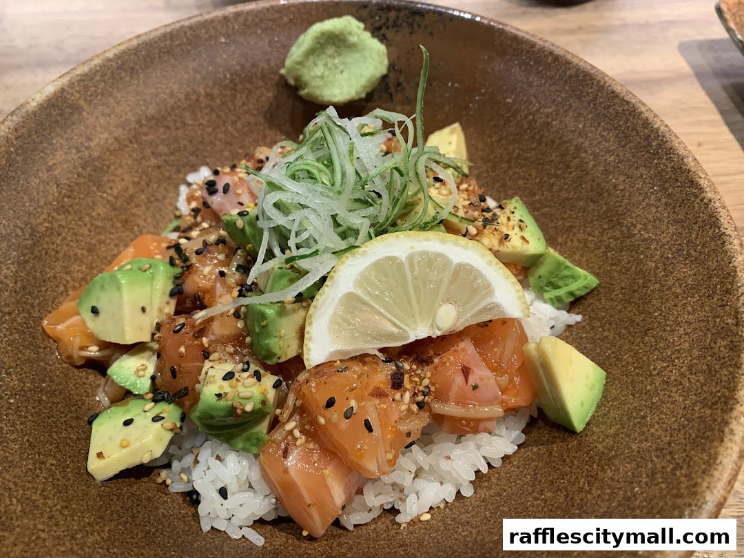A close-up of a salmon and avocado poke bowl with wasabi and lemon.