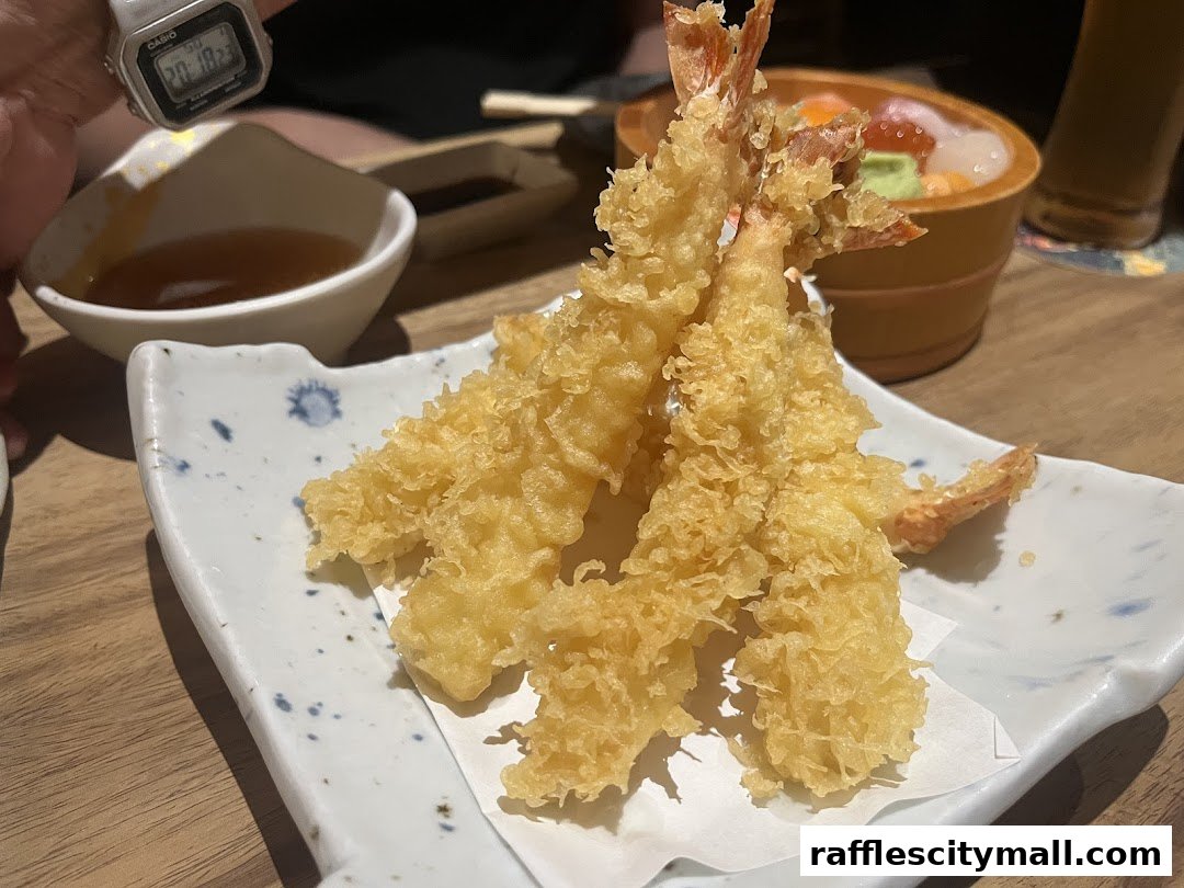 Crispy tempura shrimp served on a white plate with dipping sauce and a bowl of sashimi.