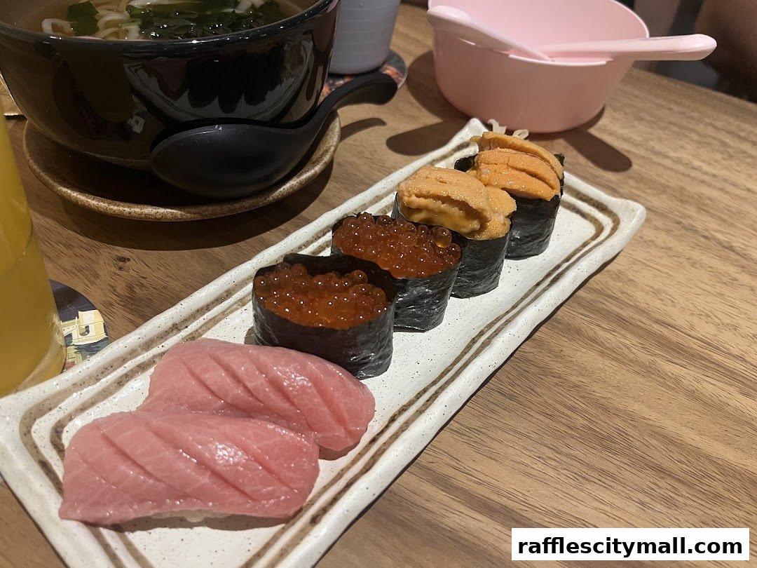 A plate of fresh sushi, including tuna and uni, with a bowl of udon noodles in the background.