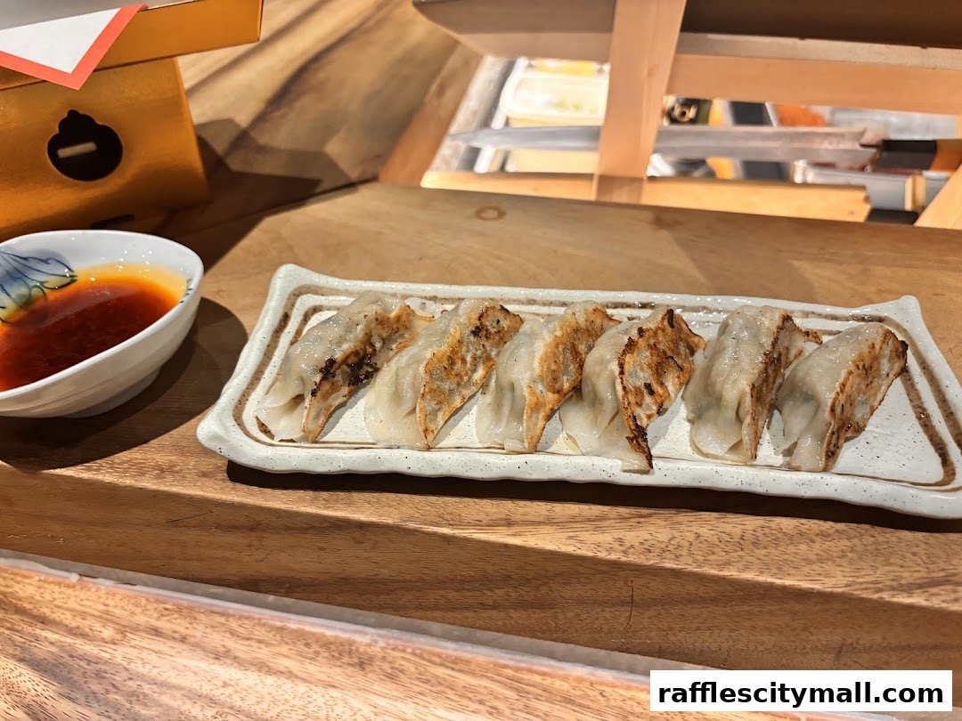 A plate of pan-fried gyoza with a side of dipping sauce on a wooden counter.