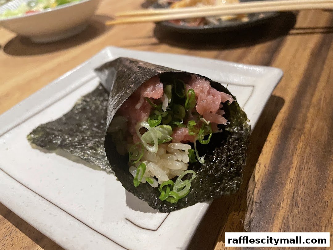 A close-up of a tuna temaki sushi roll with rice and green onions on a white plate.