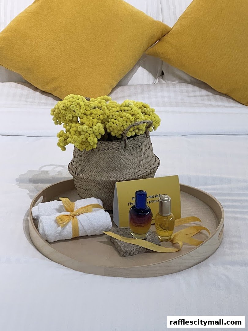 A tray with L'Occitane products, rolled towels, and yellow flowers on a bed.