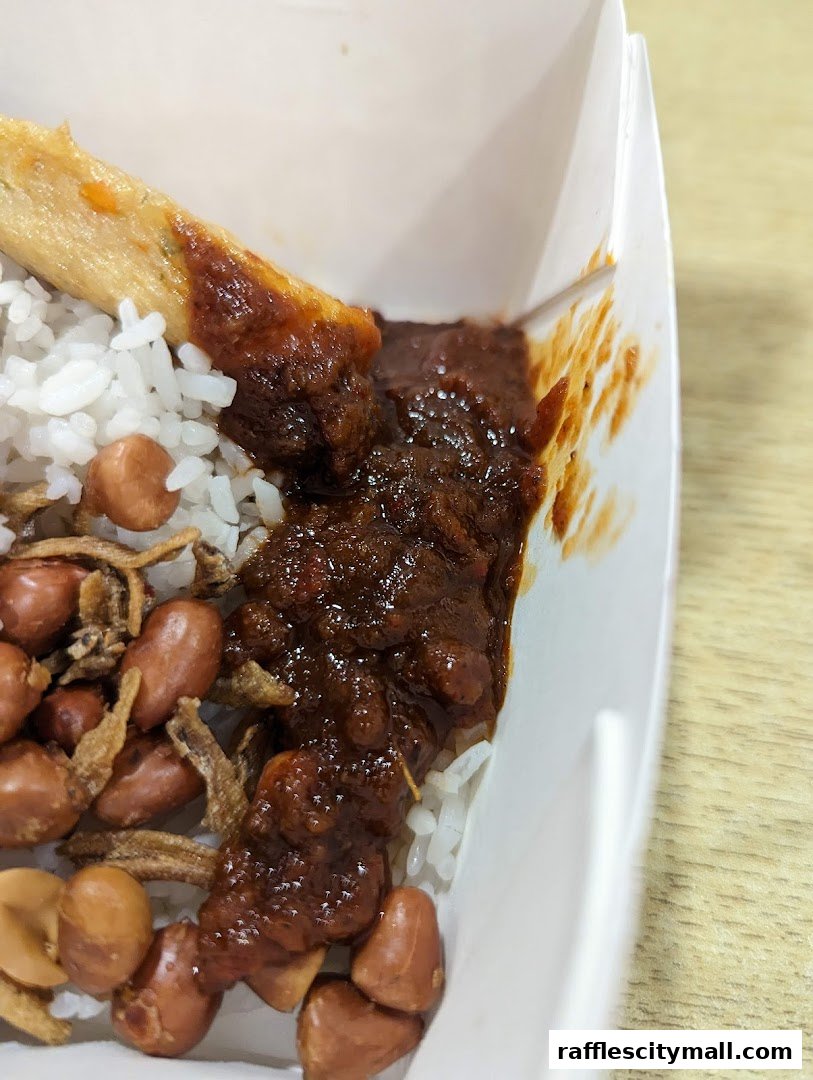 A close-up of a delicious Nasi Lemak dish with rice, sambal, peanuts, and anchovies.