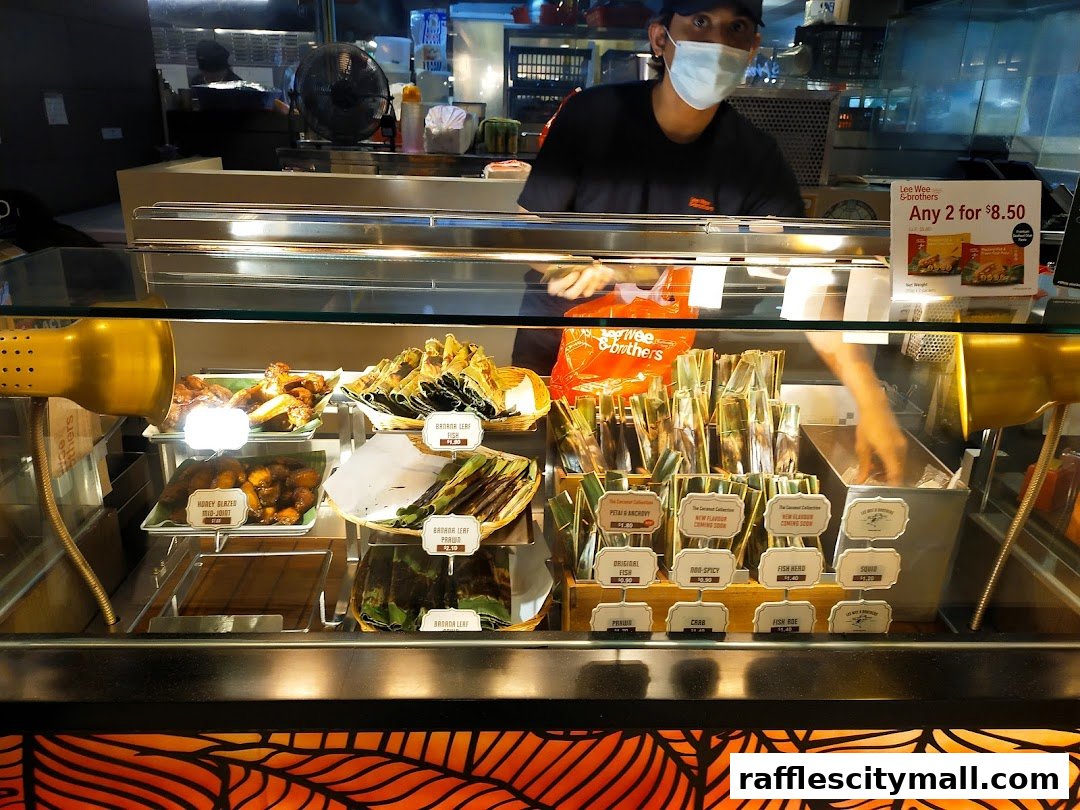 A display case filled with various food items, including grilled meats and wrapped snacks, with a staff member behind the counter.