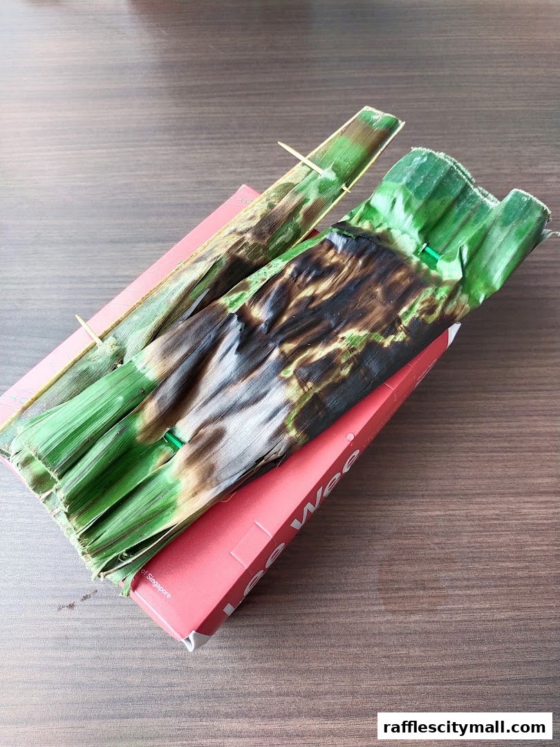 Two grilled food items wrapped in banana leaves, presented on a red box.