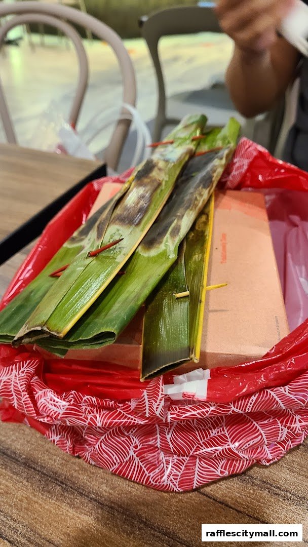 A close-up of grilled fish cakes wrapped in banana leaves, presented in a red bag.