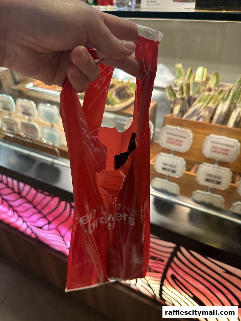 A hand holds a red plastic bag with the Lee Wee Brothers logo in front of a display case.