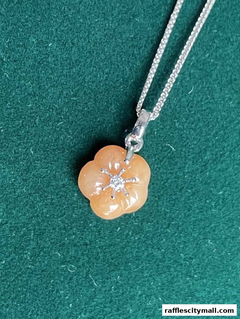 A close-up of a delicate peach-colored jade flower pendant with a diamond accent on a silver chain.