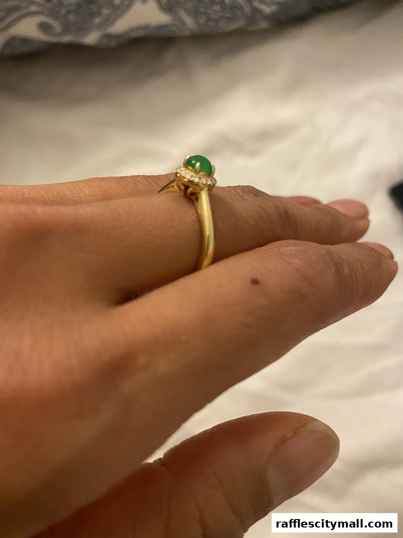 A close-up of a hand wearing a gold ring with a green jade stone and diamonds.