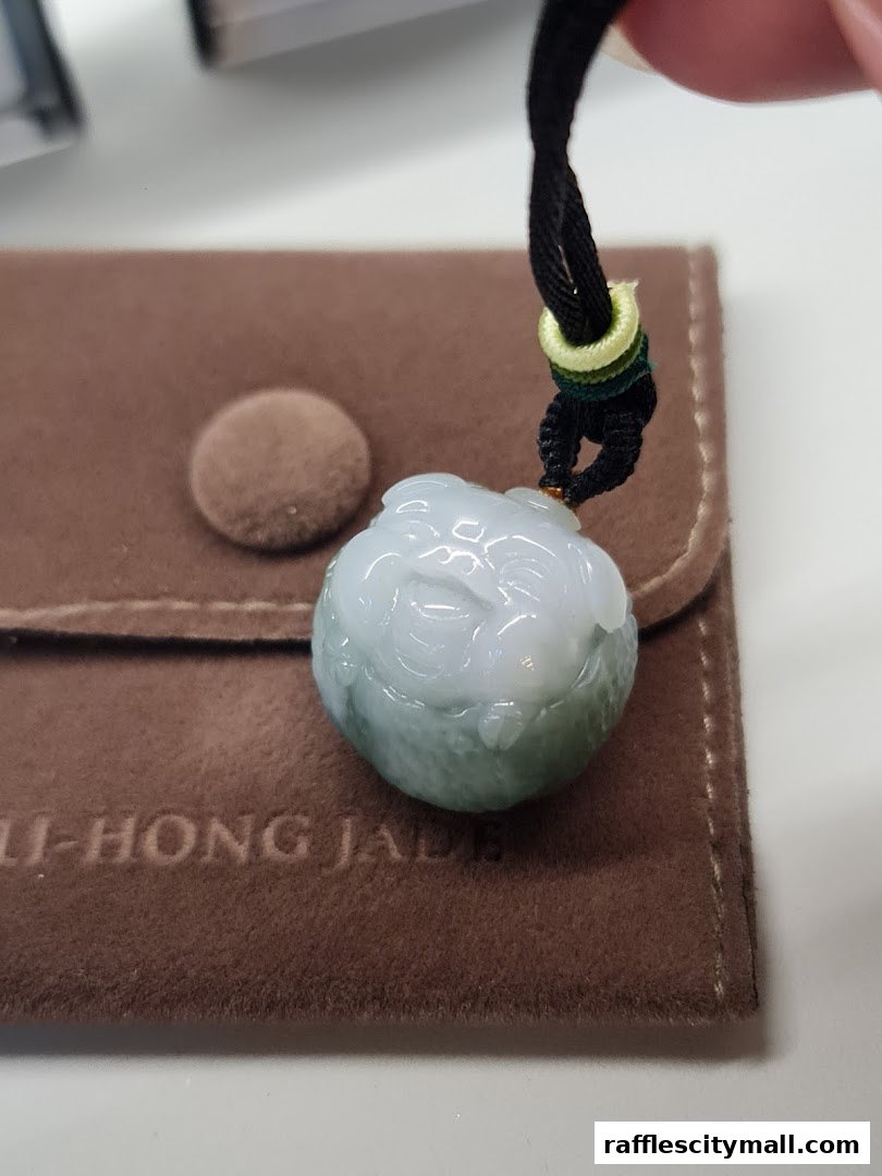 A close-up of a jade pendant with intricate carving, resting on a brown pouch.