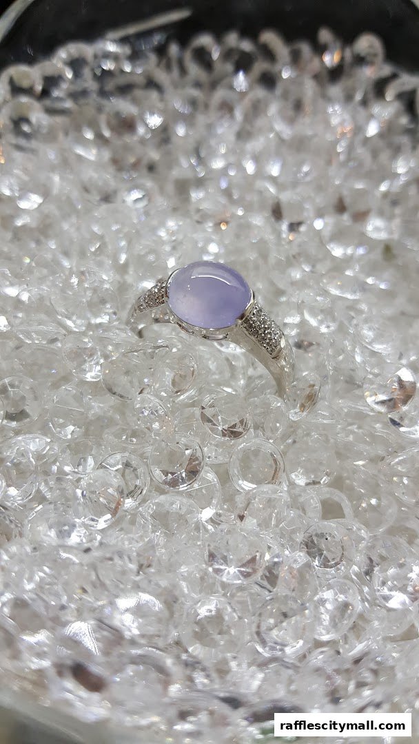 A close-up of a silver ring with a lavender jade stone and small diamonds.
