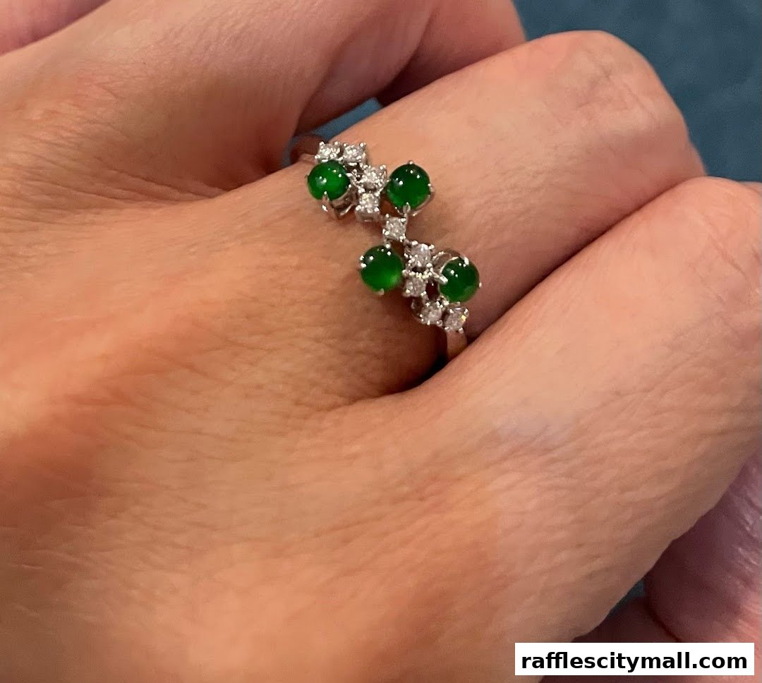 A hand wearing a delicate silver ring adorned with green jade stones and small diamonds.