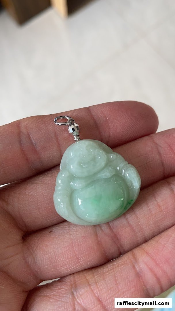 A hand holds a green jade pendant carved into a laughing Buddha.