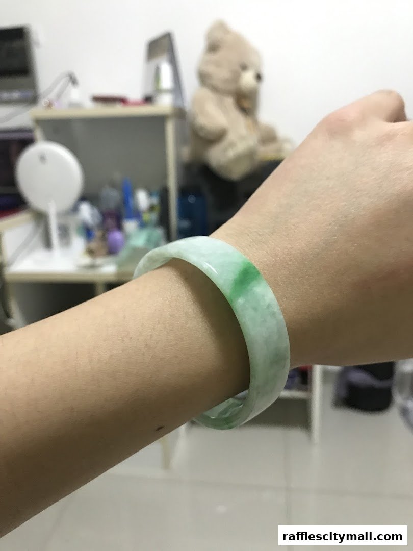 A close-up of a jade bangle on a person's wrist, with a blurred background.