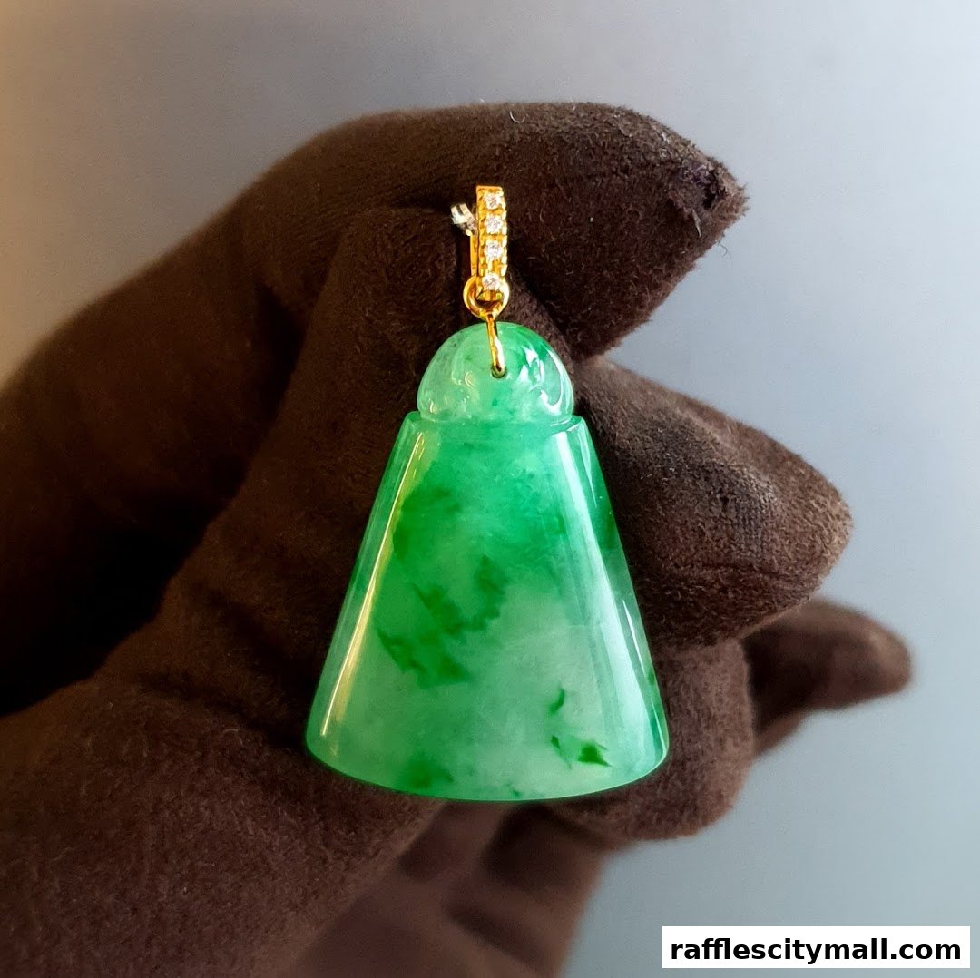 A gloved hand holds a vibrant green jade pendant with gold and diamond accents.