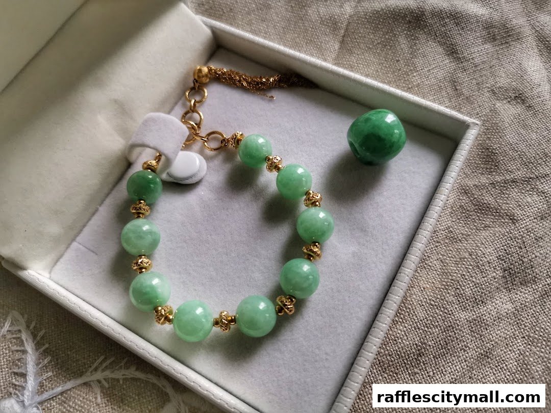 A jade bracelet with gold accents displayed in a white box, next to a loose jade bead.