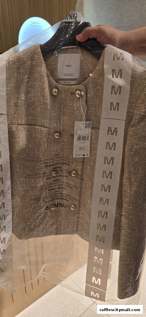 A person holds a beige tweed jacket from MANGO, packaged in plastic.