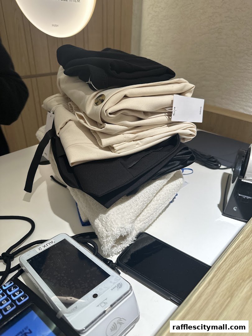 A stack of folded clothing items, including trousers and a sweater, on a counter with payment devices.
