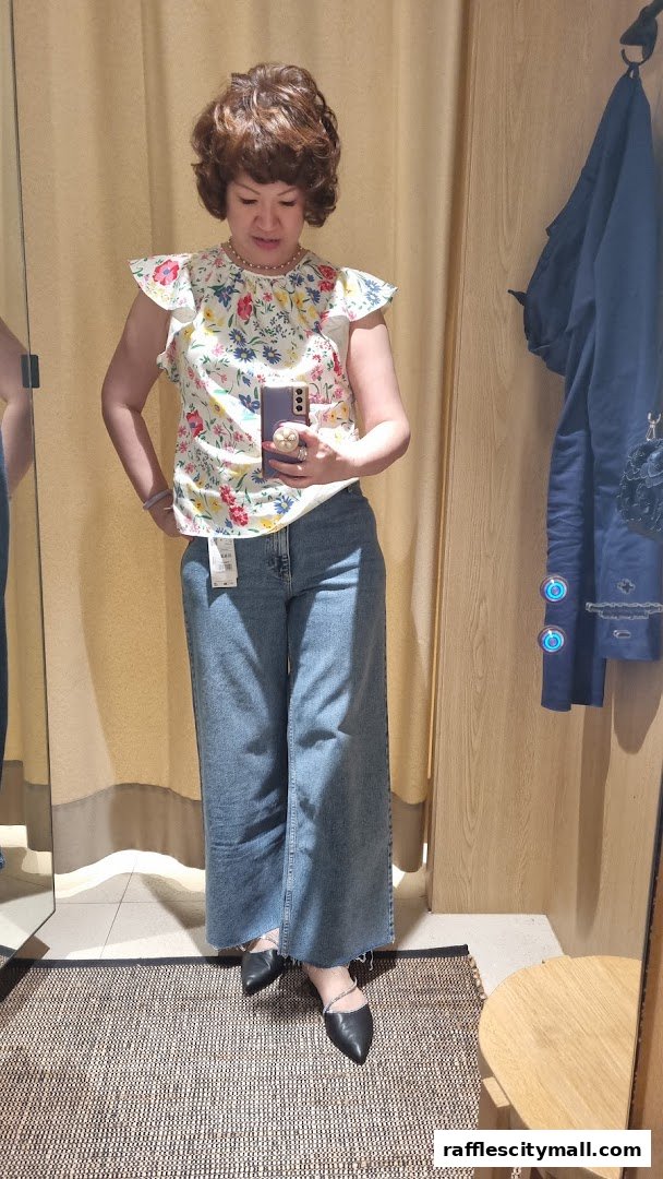 A woman tries on a floral top and wide-leg jeans in a fitting room.