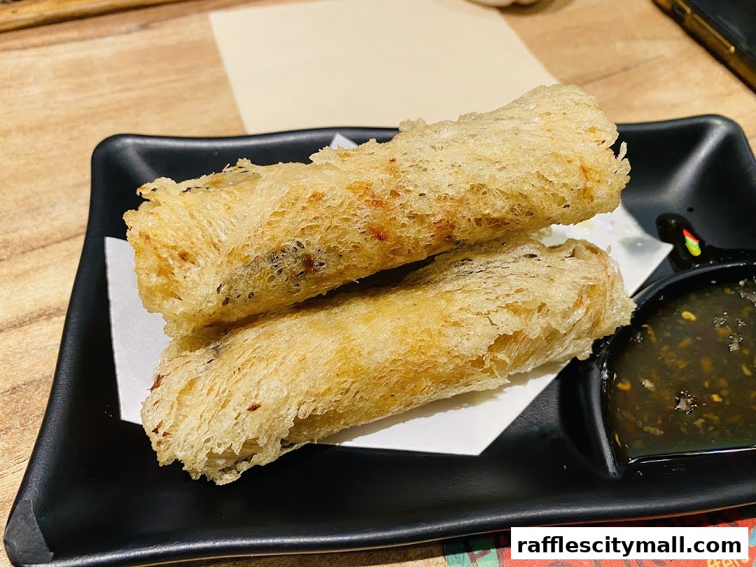 Crispy fried spring rolls served with a dipping sauce on a black plate.