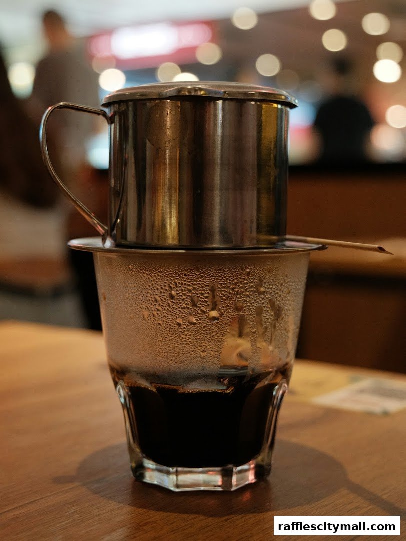 A close-up of a Vietnamese coffee being brewed in a traditional metal filter over a glass.