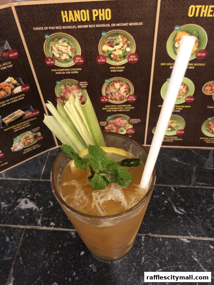 A refreshing drink with mint and lemon sits in front of a menu featuring Vietnamese pho dishes.