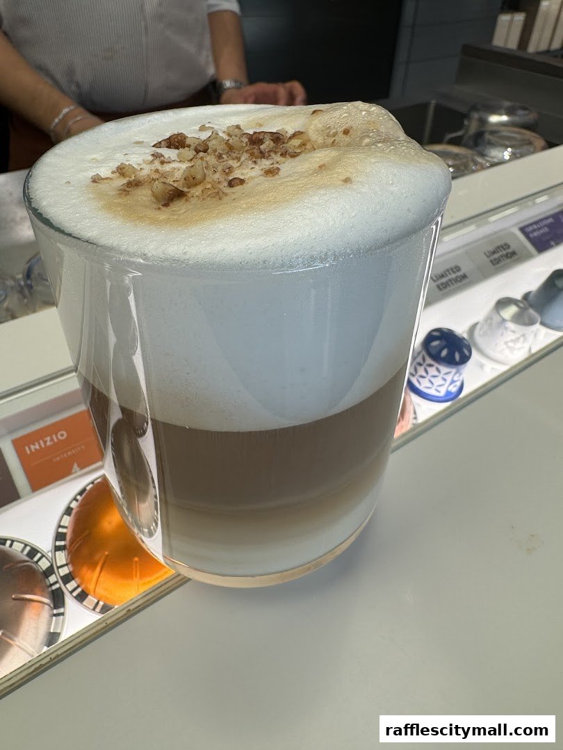 A layered coffee drink with foam and nuts in a glass, with Nespresso pods visible.
