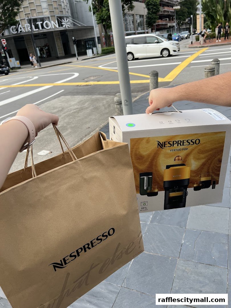 Hands holding a Nespresso shopping bag and a Vertuo Pop coffee machine box.