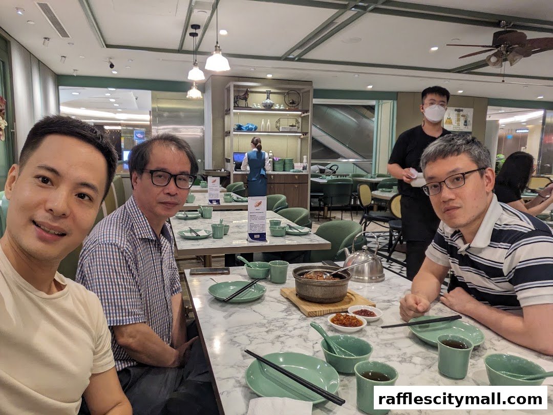 Four men are seated at a table in a restaurant, with food and drinks laid out.