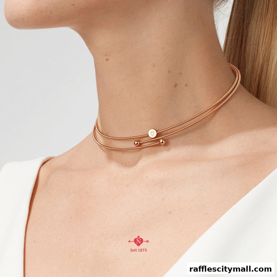 A close-up of a woman wearing a rose gold choker necklace with a heart charm.