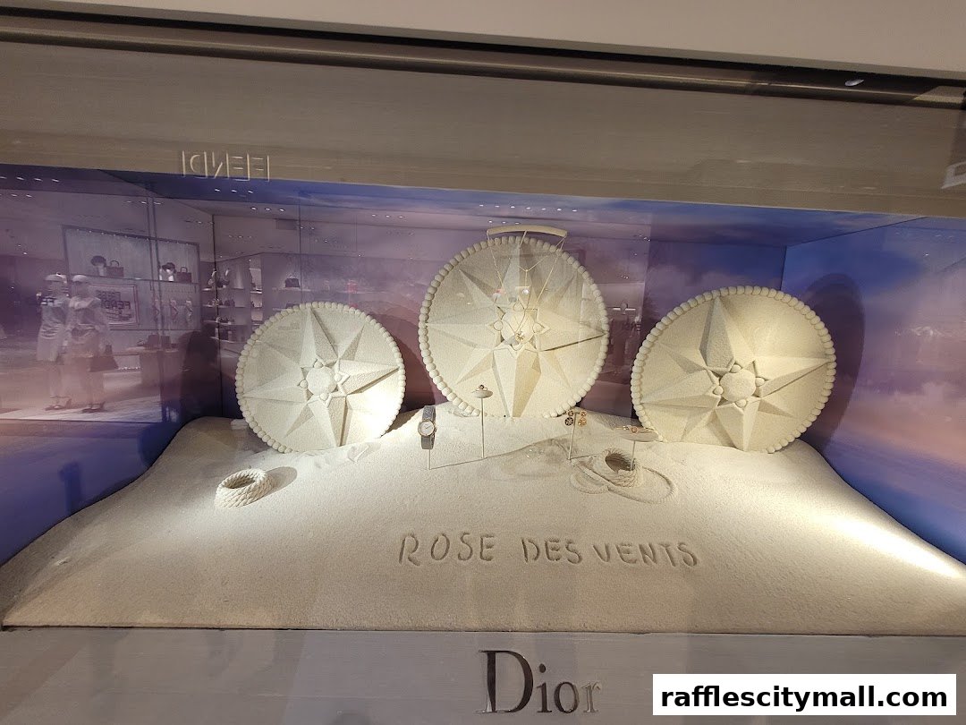 Dior store window display featuring Rose des Vents jewelry and compass motifs on a sandy beach theme.
