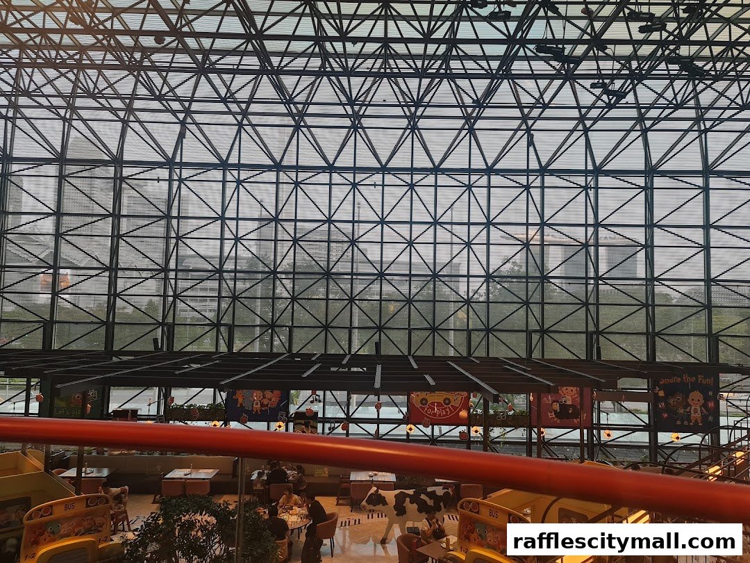 Interior view of a cafe with a large glass ceiling and metal structure, showing seating areas.