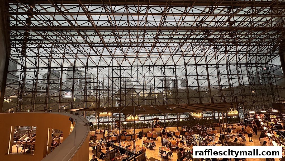 Interior view of a bustling cafe with many patrons seated at tables under a large, geometric glass ceiling.