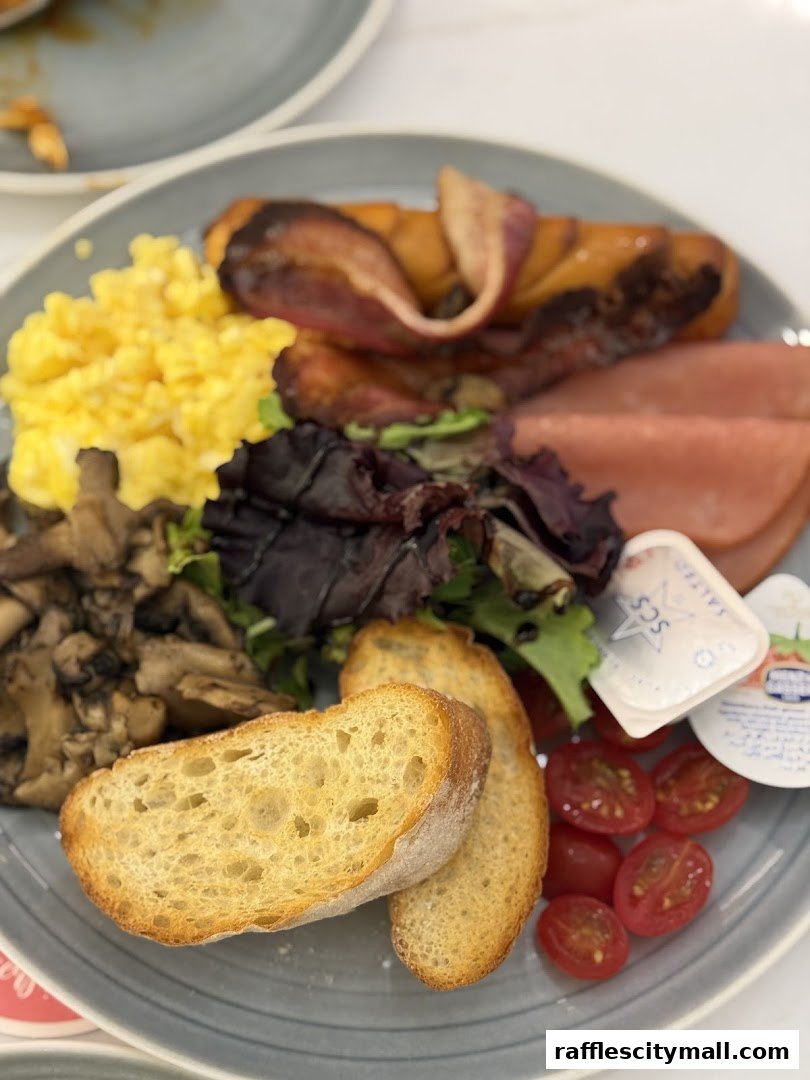 A plate of breakfast food including scrambled eggs, bacon, ham, mushrooms, bread, and tomatoes.