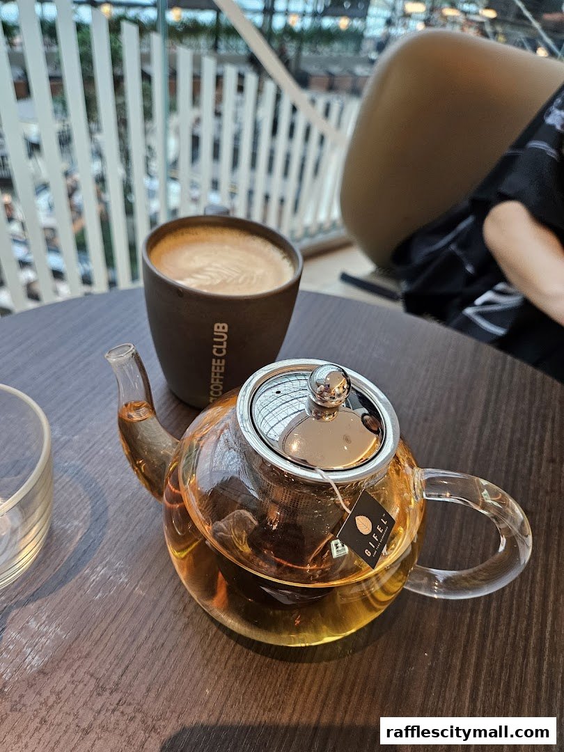 A glass teapot filled with amber liquid sits next to a coffee cup on a wooden table.