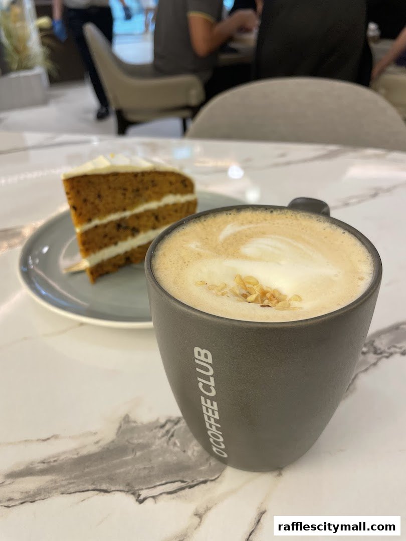 A cup of coffee with latte art and a slice of cake on a marble table.
