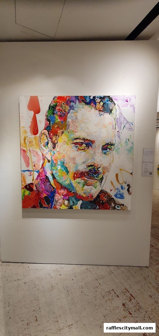 A vibrant, textured portrait of Freddie Mercury hangs on a white wall in an art gallery.