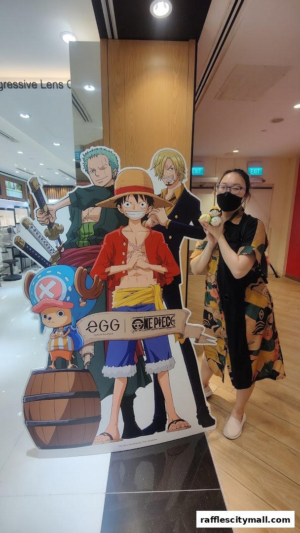 A woman poses with a One Piece character cutout and plush toys at Optical 88.