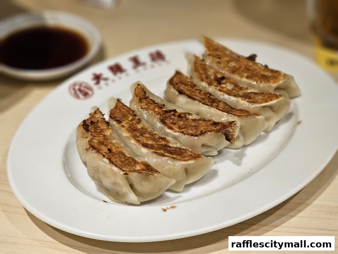 A plate of golden-brown pan-fried gyoza dumplings with a side of dipping sauce.