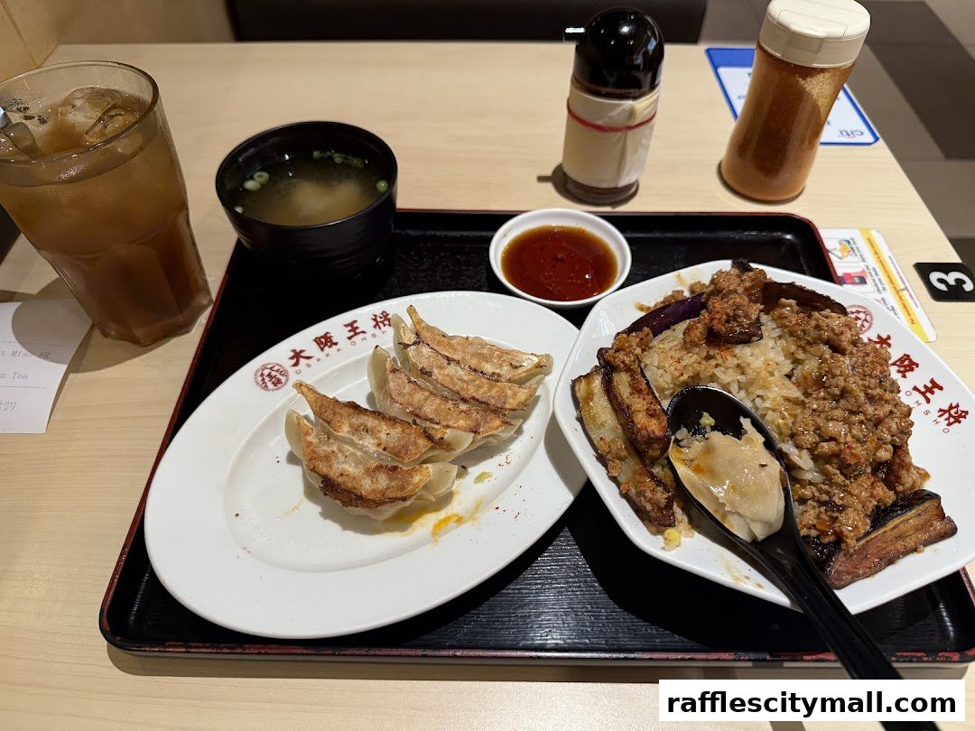 A meal at Osaka Ohsho featuring gyoza, a rice dish with eggplant and minced meat, miso soup, and iced tea.
