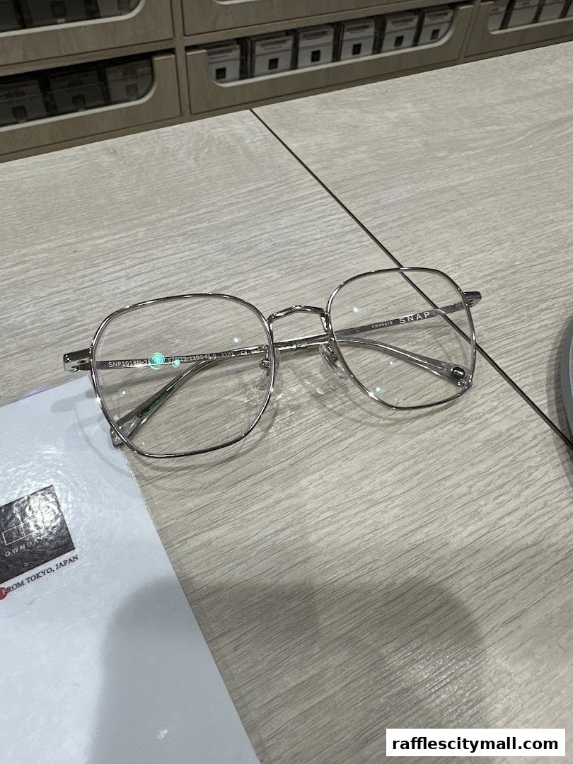 A pair of stylish silver-rimmed glasses rests on a light wooden surface next to a brochure.