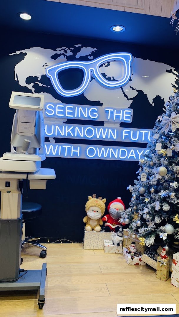 Interior of OWNDAYS Raffles City with a neon sign, eye testing equipment, and a Christmas tree.