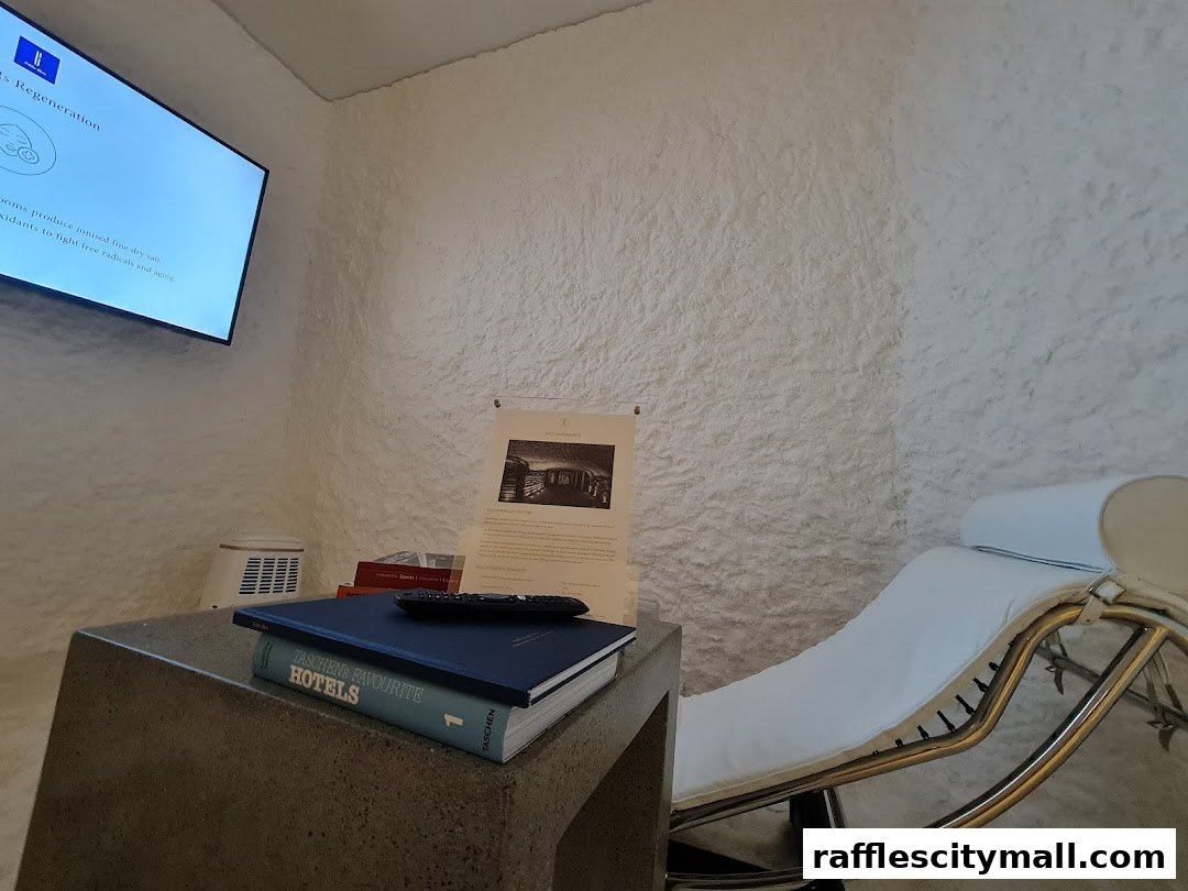 A relaxation room with a chaise lounge, a screen displaying health information, and books on a table.