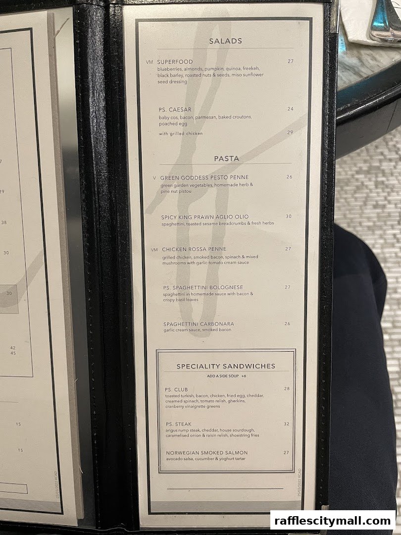 A close-up view of a restaurant menu featuring salads, pasta, and sandwiches.