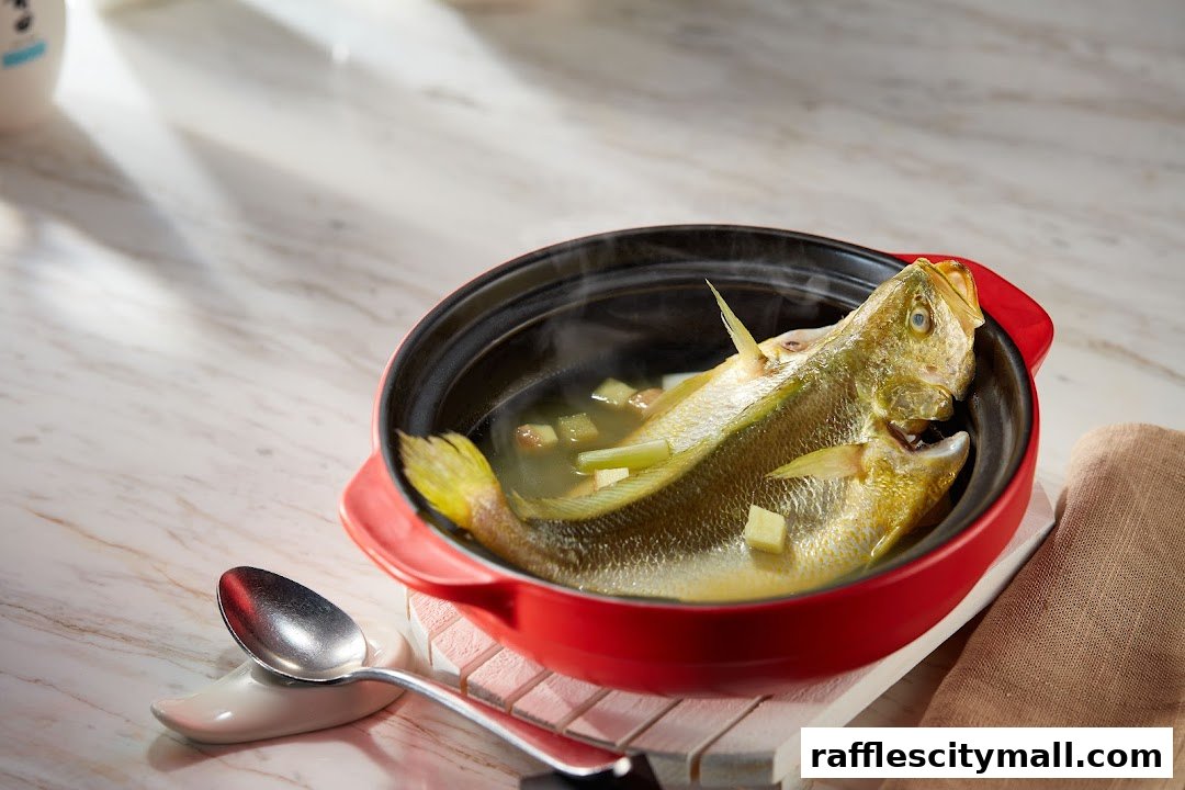 A whole steamed fish in a red pot with ginger and scallions, served with a spoon.
