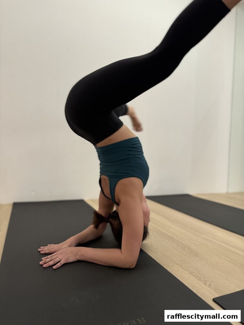 A woman performs a yoga headstand on a mat in a studio.
