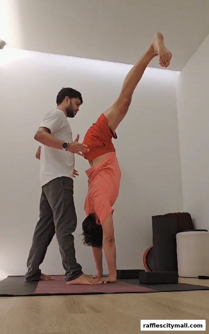 A yoga instructor assists a student in performing a handstand on a yoga mat.