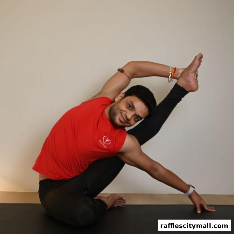 A man in a red t-shirt and black leggings performs a yoga pose on a mat.